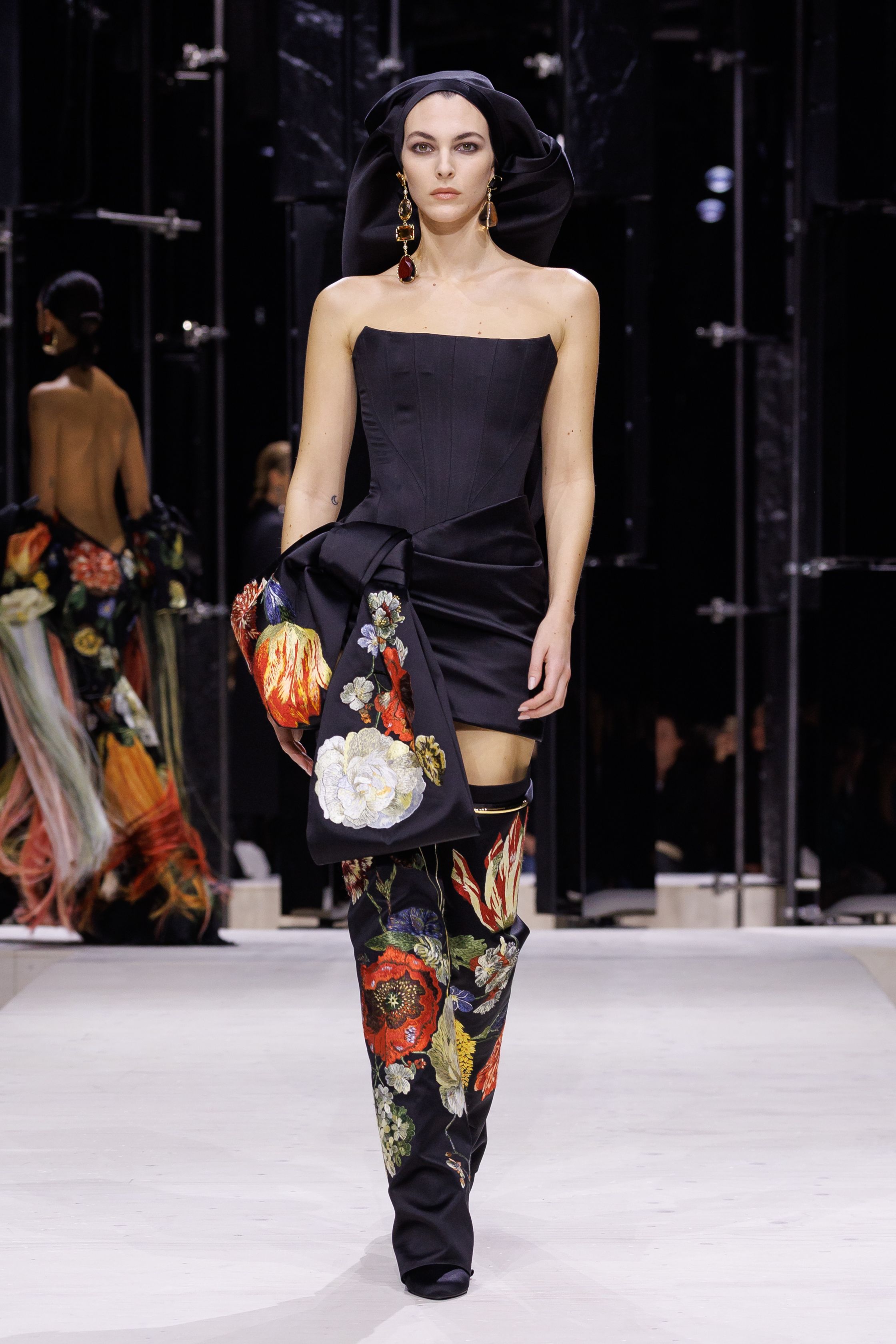 Givenchy 2026秋冬在现代建筑空间中呈现一场充满戏剧性的时装叙事：雕塑式西装、亮色斗篷、结构礼服与夸张装饰共同构建品牌标志性的高级时装气质。蓝色、红色与黄色的高饱和色彩与黑白经典形成鲜明对比，服装通过立体剪裁与夸张廓形展现出强烈视觉张力。整场系列在优雅与戏剧之间取得平衡，展现现代高级时装的力量-顽石频道趋势研究